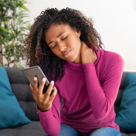 Junge schwarze Frau mit Schmerzen vom Handynacken hält sich den Hals und sieht schmerzgeplagt aus.