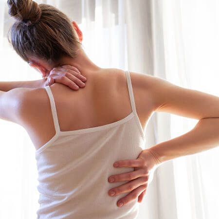 Junge blonde Frau mit Schmerzen von Hausarbeiten hält sich den Nacken und den Rücken.