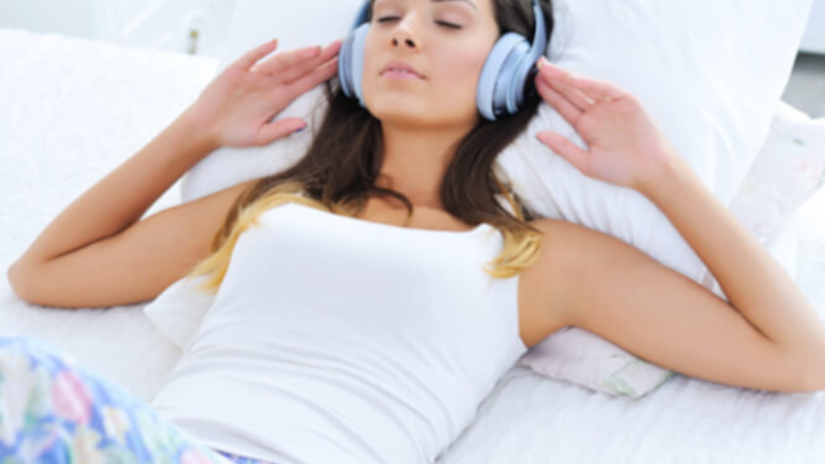 Eine junge dunkelhaarige Frau liegt entspannt auf dem Rücken und genießt mit geschlossenen Augen die Musik aus ihrem Kopfhörer.