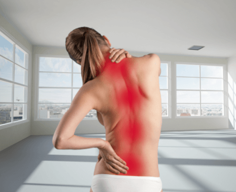 Eine junge blonde Frau steht mit dem Rücken zum Betrachter und hält sich mit einer Hand den Nacken und der anderen den unteren Rücken. Mehrere großflächige rote Punkte stellen die Schmerzen im ganzen Rücken dar.