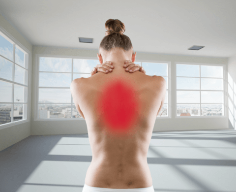 Eine junge, blonde Frau steht mit dem Rücken zum Betrachter. Sie blickt nach unten und hält sich mit beiden Händen den Nacken. Ein großflächiger roter Punkt stellt die Schmerzen im oberen Rücken dar.