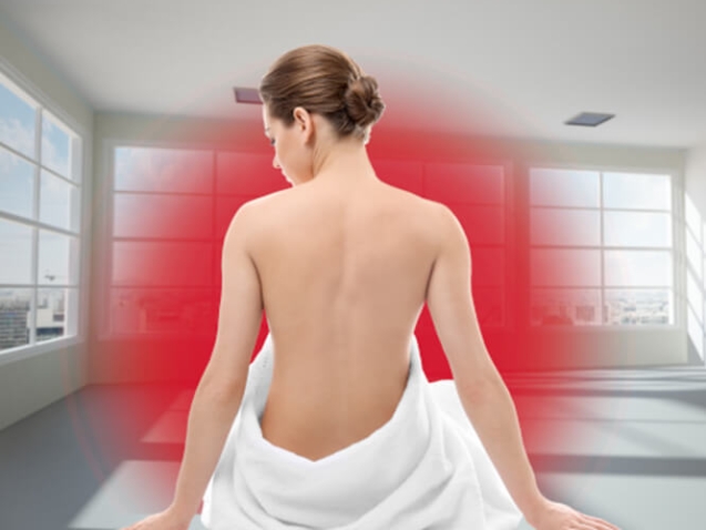 Eine junge blonde Frau sitzt mit dem Rücken zum Betrachter auf dem Boden. Sie ist bis zur Hüfte in ein weißes Handtuch gewickelt. Vor ihr ist ein roter Kreis, der die Infrarotwärme darstellt.