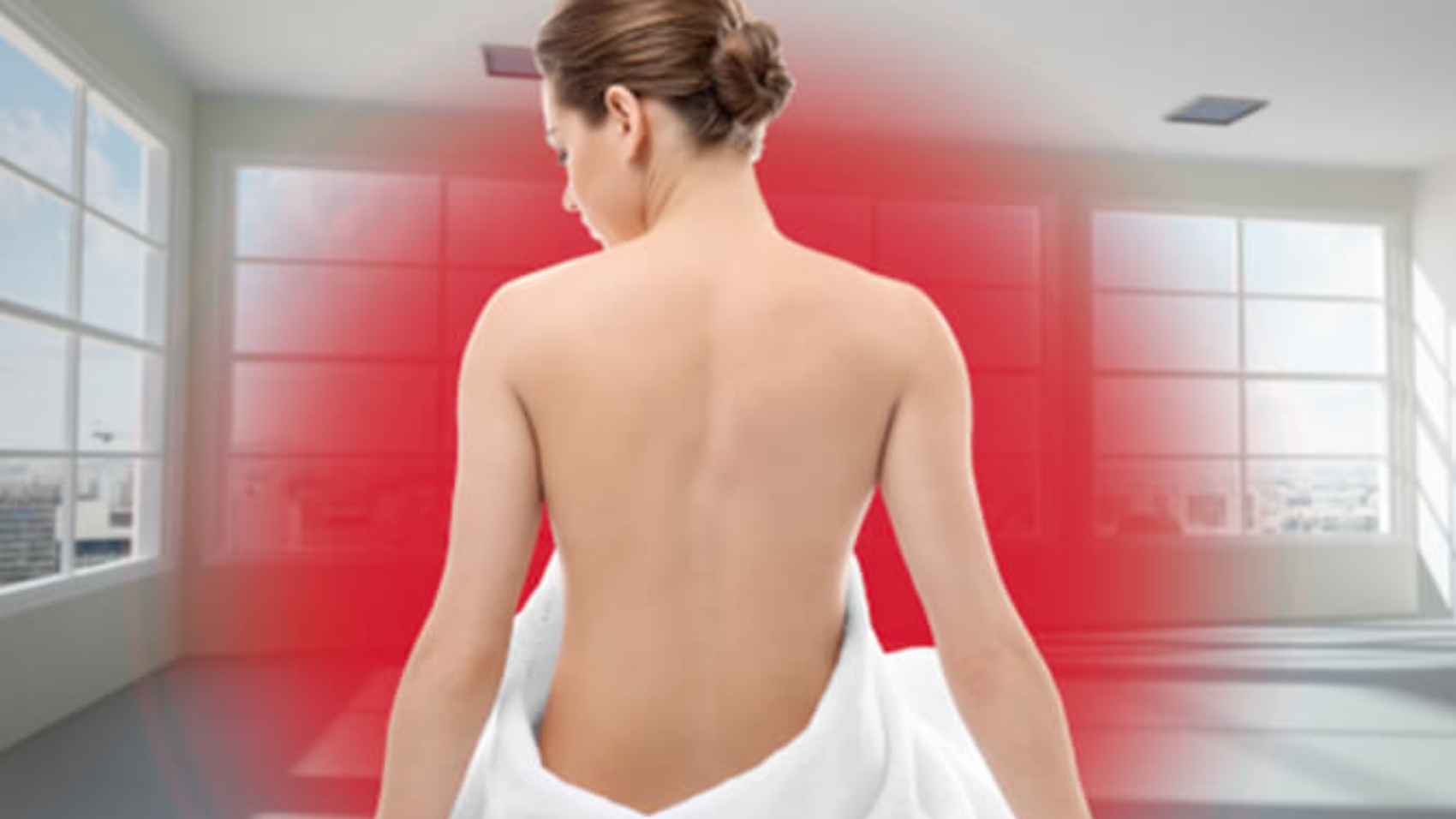 Eine junge blonde Frau sitzt mit dem Rücken zum Betrachter auf dem Boden. Sie ist bis zur Hüfte in ein weißes Handtuch gewickelt. Vor ihr ist ein roter Kreis, der die Infrarotwärme darstellt.