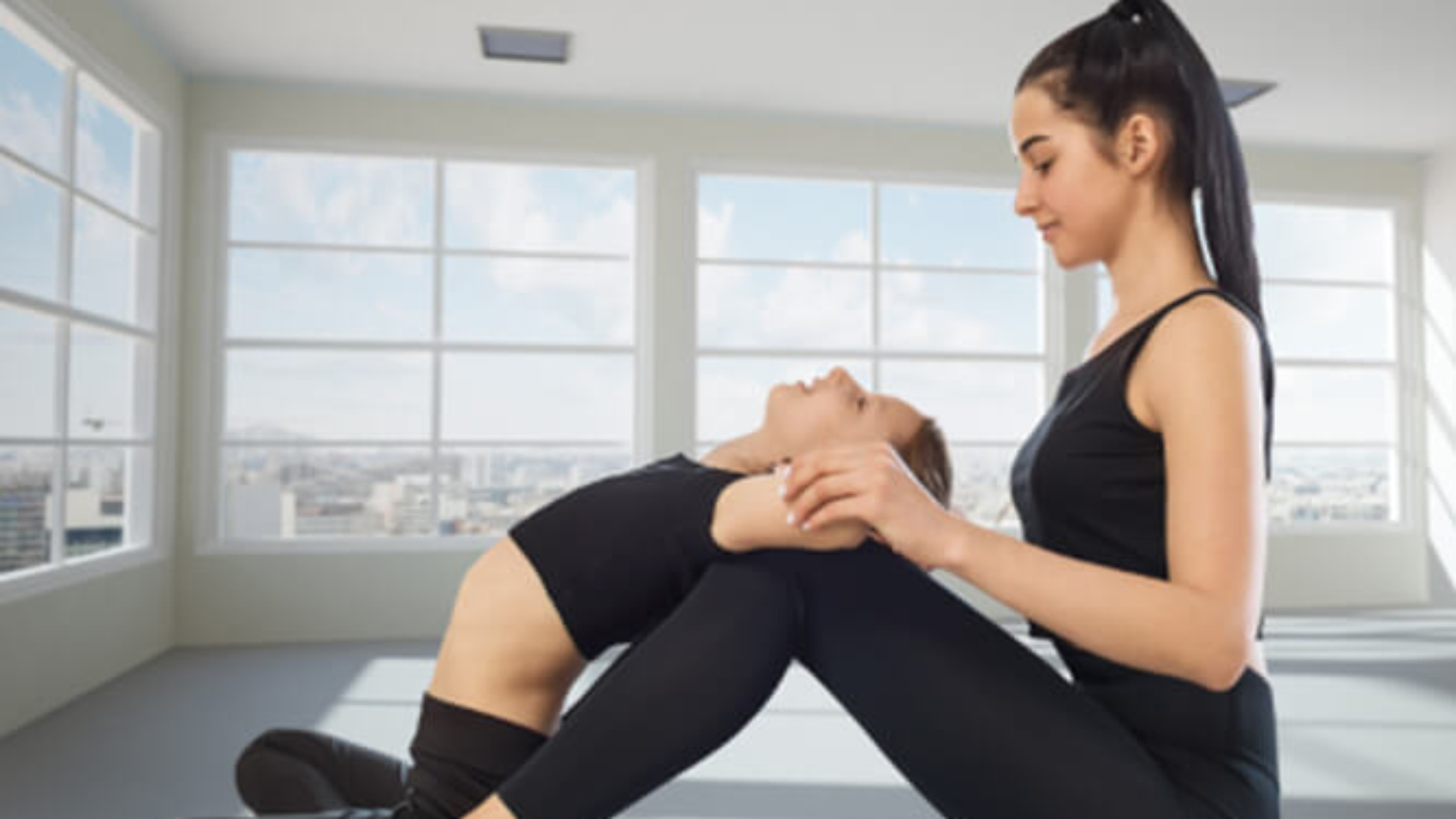 Eine junge orientalisch aussehende Frau sitzt nach links gewendet am Boden. Sie hält ein Mädchen an den Armen und streckt dessen Rücken über Ihre Knie.