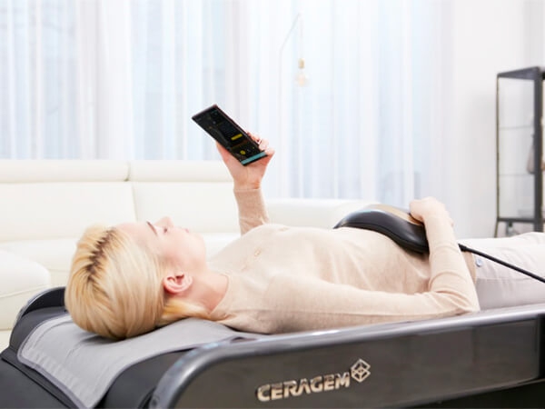Blonde Frau liegt auf der CERAGEM Master V4 Massageliege und entspannt sich mit dem Master Modus und dem Bauchmassagegerät.