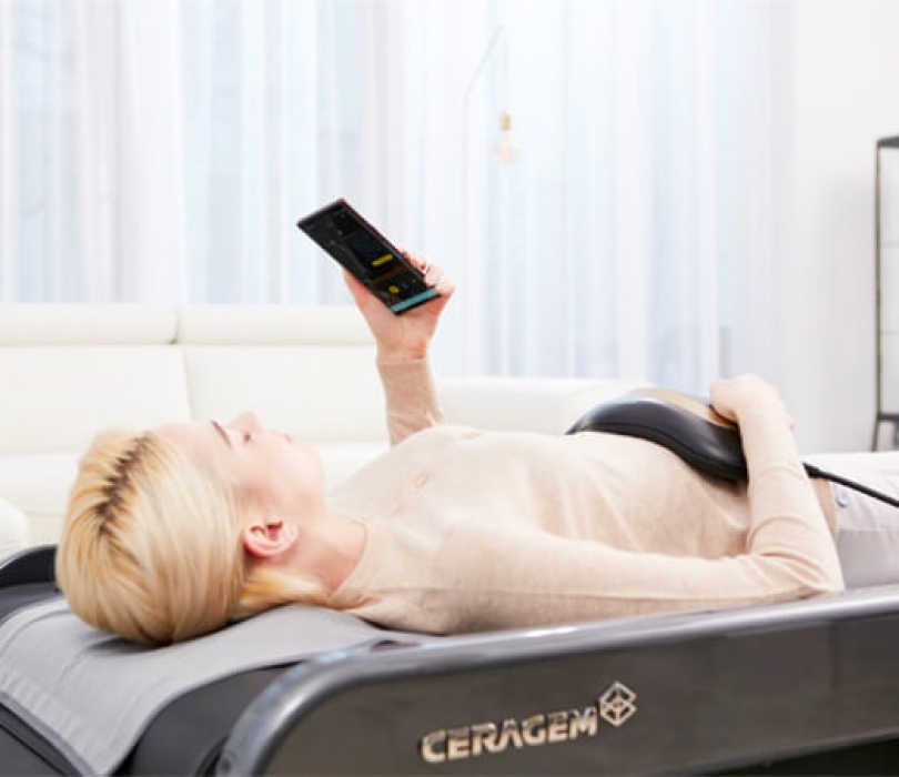 Blonde Frau liegt auf der CERAGEM Master V4 Massageliege und entspannt sich mit dem Master Modus und dem Bauchmassagegerät.