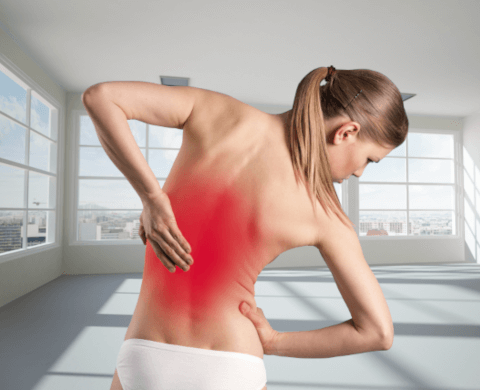 Eine junge blonde Frau beugt sich mit Rückenschmerzen nach rechts und hält sich mit beiden Händen den Rücken. Ein großflächiger roter Punkt stellt die Schmerzen im mittleren Rücken dar.