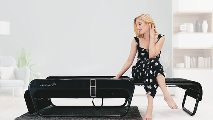 Blonde Frau sitzt auf CERAGEM Master V4 Liege und fasst das Obermaterial an.