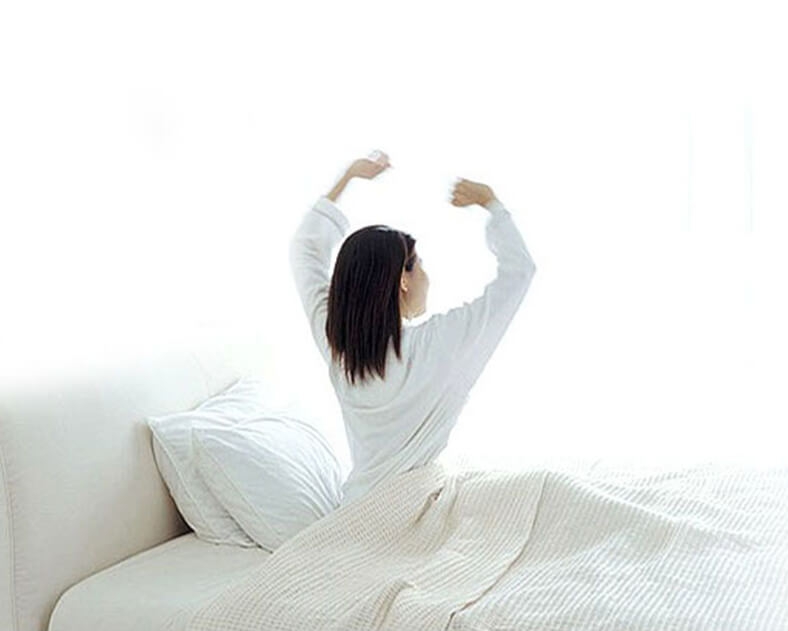 Frau im weißen Pyjama streckt sich erholt auf dem Bett.