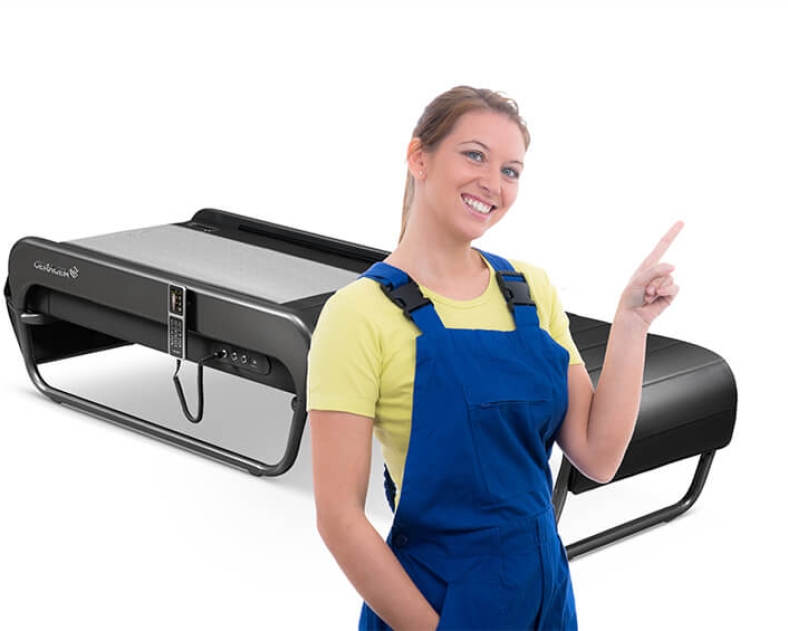 Junge blonde Frau im Blaumann steht vor V4 Liege, lächelt und weist mit dem Zeigefinder auf den Dialogbereich auf der rechten Seite hin.