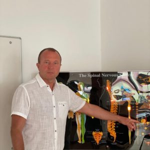 Wjatscheslaw Trippel, CERAGEM-Center-Inhaber Würzburg, steht vor einer Informationstafel auf der eine Wirbelsäule zu sehen ist.